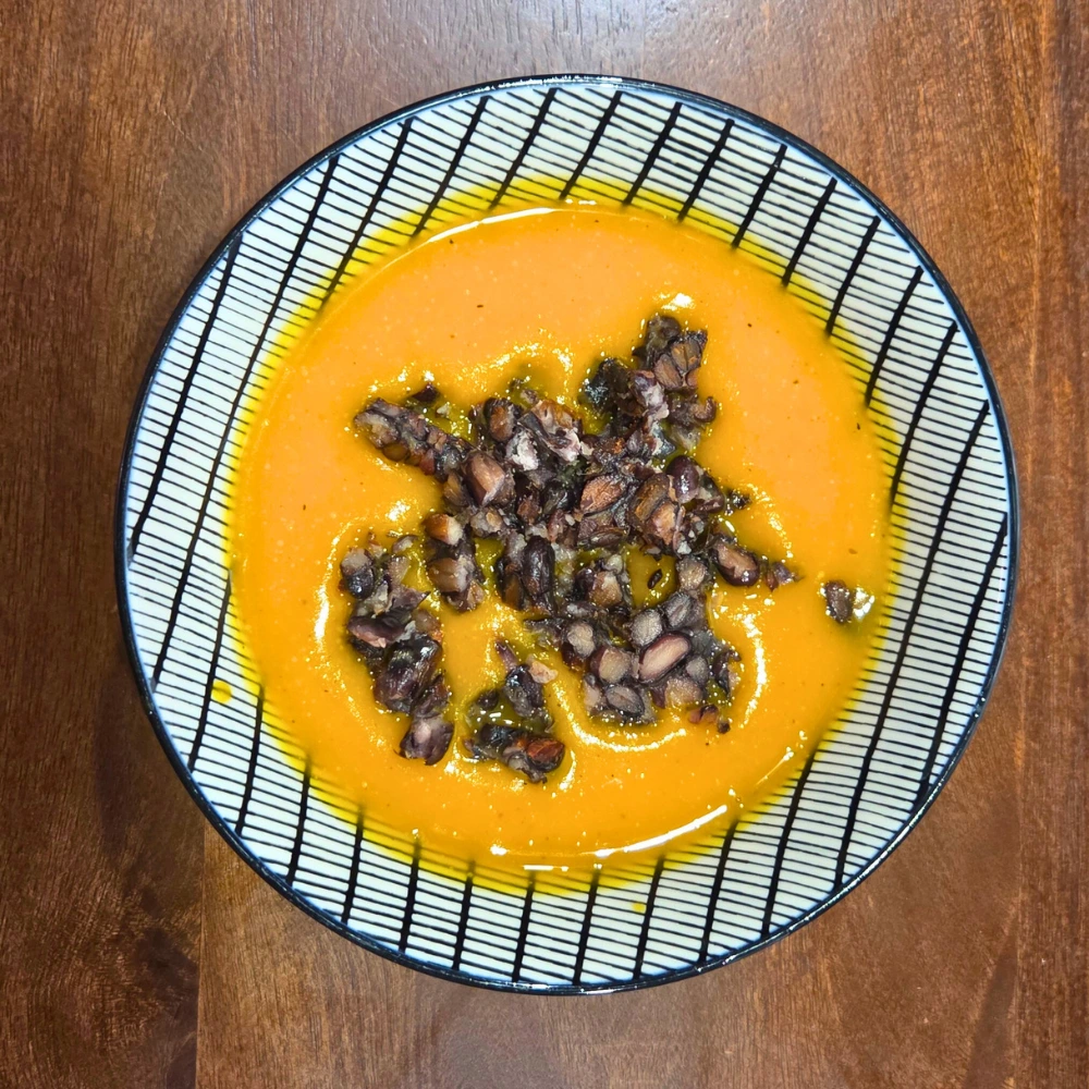 Cremige Kürbissuppe mit knusprigem Tempeh-Crumble in einer dekorativen Schale auf Holztisch